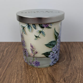 A soy wax candle in a glass jar with a floral design, including a lid with a metal emblem.