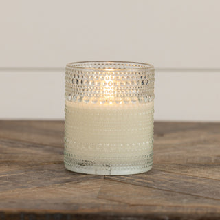 Clear hobnob glass flameless flickering candle glowing softly on a white surface – JSQ Mercantile, Women’s Boutique & Gift Shop in La Grange, IL.