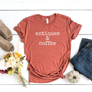 Red t-shirt with 'antiques & coffee' text on a white wooden surface with accessories.