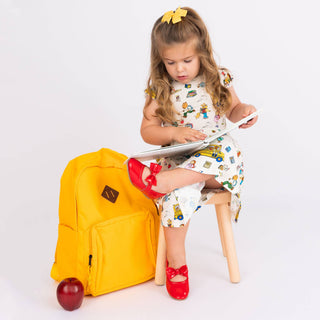 Child sitting on a stool with a tablet next to a yellow backpack on a white background