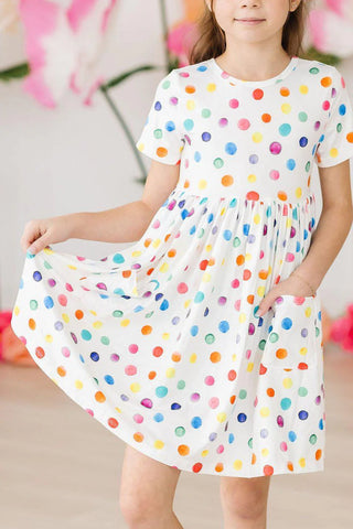 Child wearing a white dress with colorful polka dots against a blurred floral background