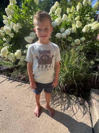 Child standing on a sidewalk next to greenery with white flowers