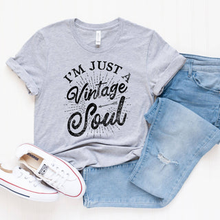 Gray t-shirt with 'I'm Just a Vintage Soul' text, blue jeans, and white sneakers on a white background