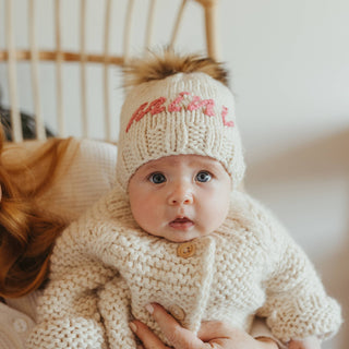 Mini Embroidered Toddler Hat with Brown Pom Pom – Hand-knit baby hat with “Mini” in cerise pink yarn. Sustainable and gift-ready. Available at JSQ Mercantile in La Grange, IL.
