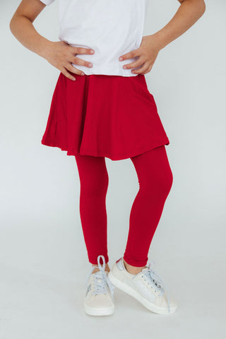 Kid wearing a white top, red skirt, and red leggings with white sneakers on a light gray background