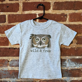 Gray t-shirt with owl graphic and 'wild & free' text on a brick wall background